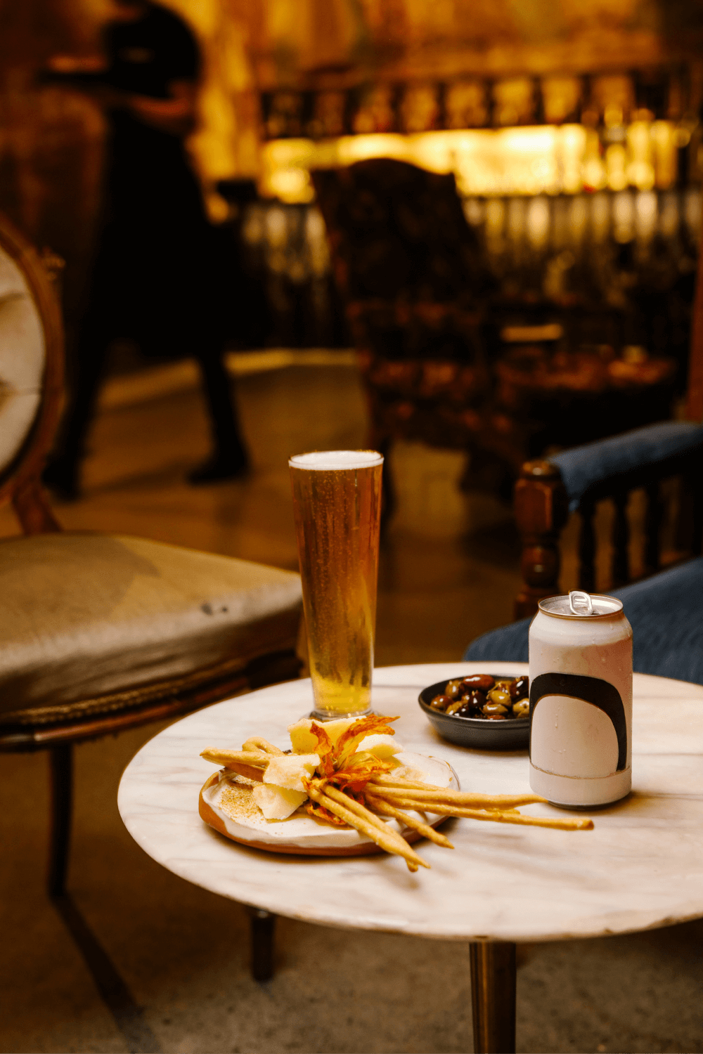 A table set with a tall Moo Brew beer, grissini and olives