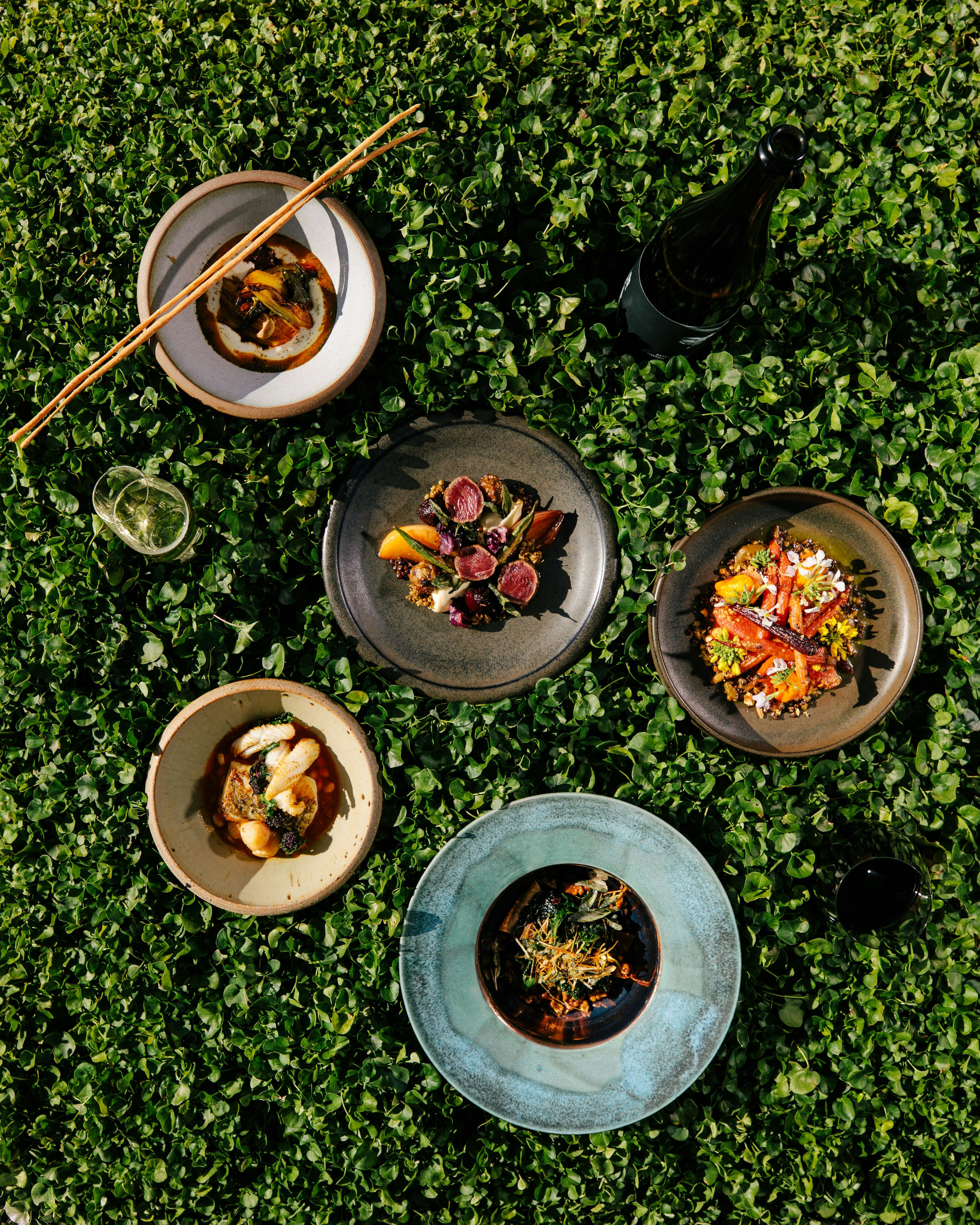 5 plates of colourful food sit in ceramic dishes on top of a bed of living clover.