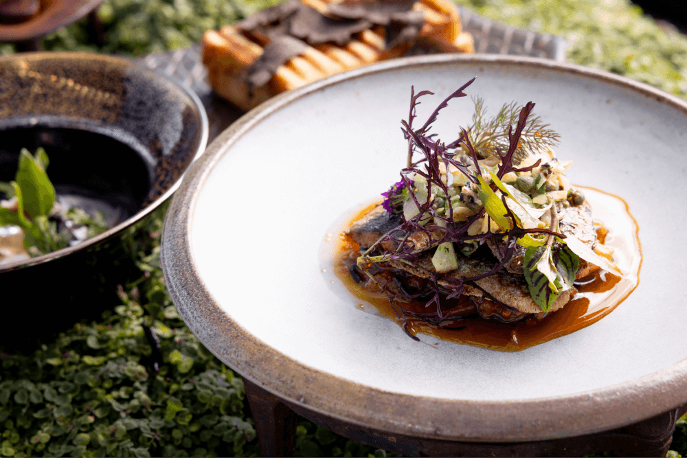 A ceramic plate with a dish dressed with delicate green and purple leaves and a vibrant orange sauce