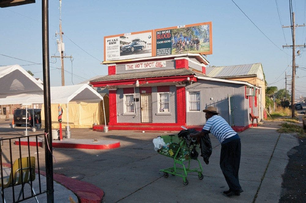 A person pushing a stopping trolley past what used to be a petrol station with a banner saying "THE HOT SPOT" on the front