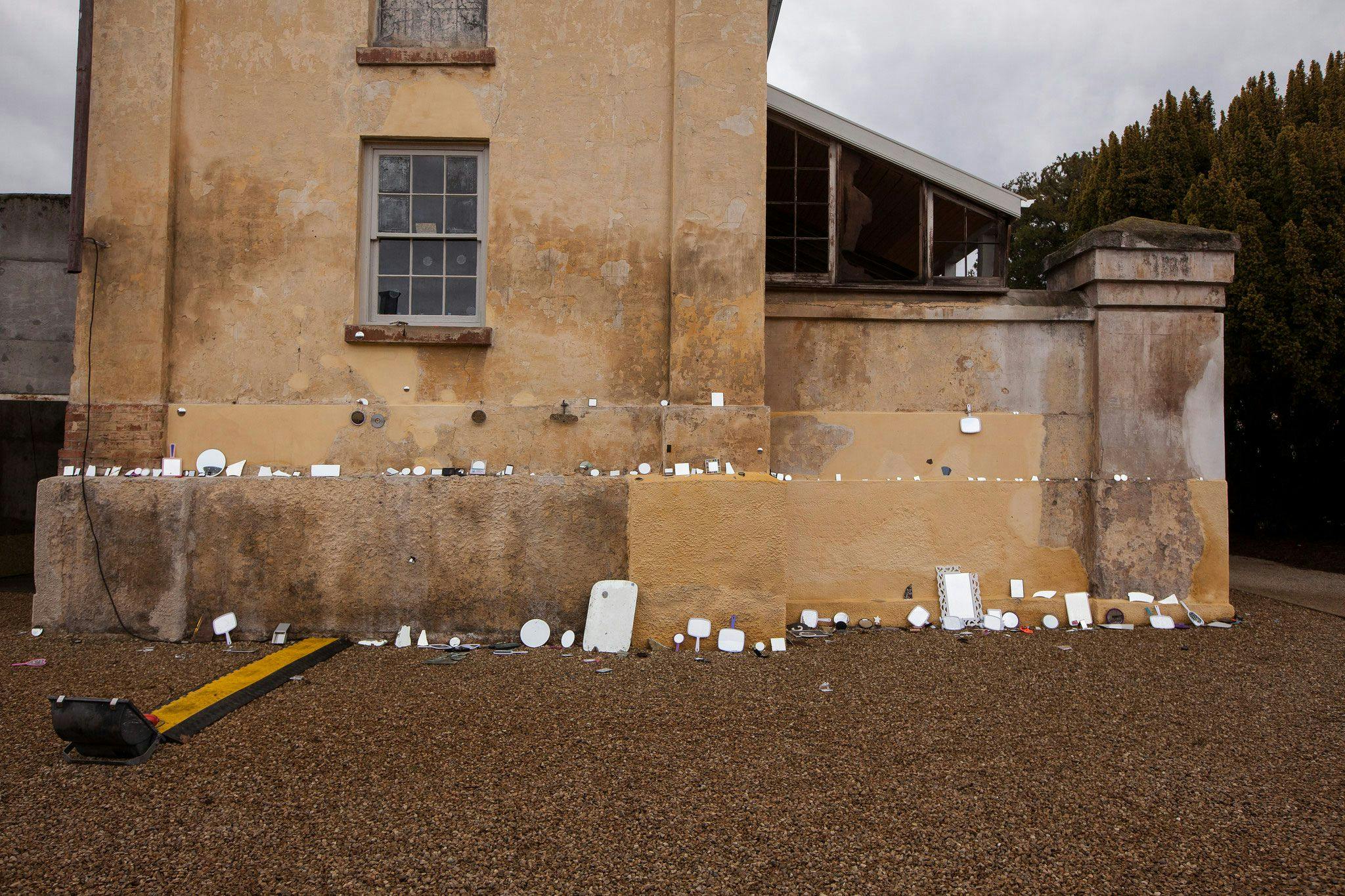 A colonial sandstone building with rows of mirrors of various sizes leaning up against it.