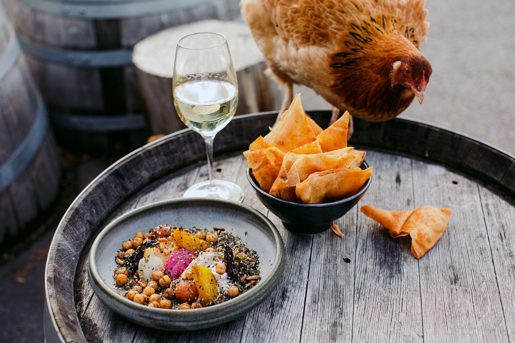 A chicken eyes off plates of chickpeas and chips