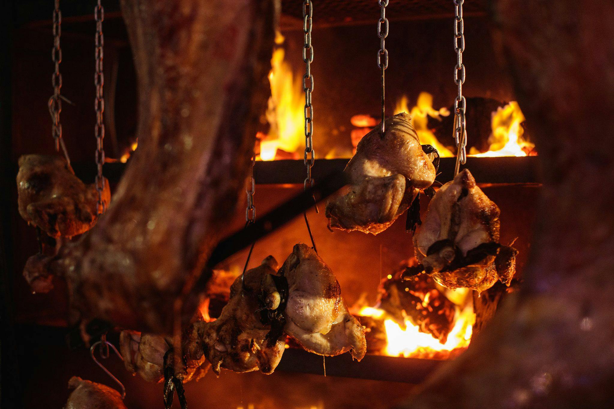 Whole chickens hanging from chains cooked over a tiered grill