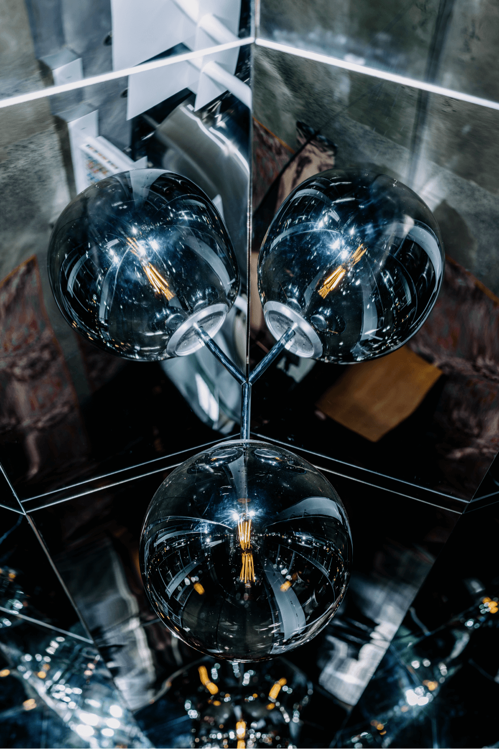 A shiny round light globe with an orange element reflecting off two mirrors